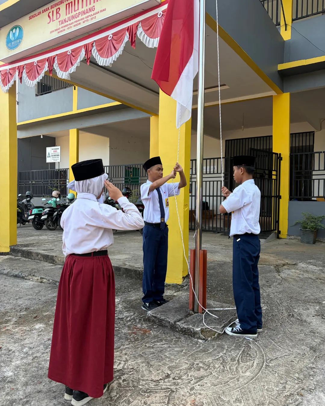 Siswa mengibarkan bendera di depan sekolah